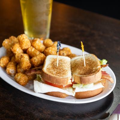 BLT sandwich served with tater tots and paired with a glass of beer.
