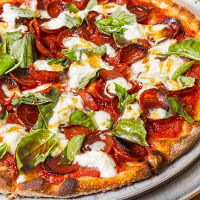 Close-up of a pepperoni pizza topped with mozzarella, hot honey, and basil.