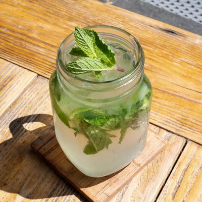 Mint lemonade in a mason jar on a sunlit wooden table.