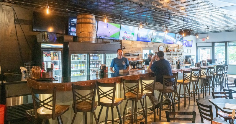 Interior, a bar with multiple TVs, bar staff and a customer sitting  at the counter