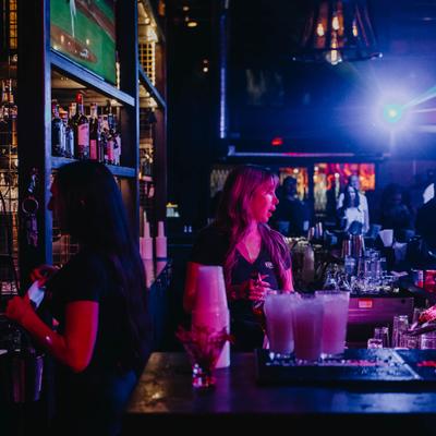 Dimly lit bar interior with a glowing back-bar shelf of liquor bottles and a bar counter.