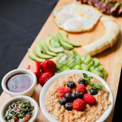 Deluxe board with sliced steak, fried eggs, oatmeal topped with berries and fresh fruit.