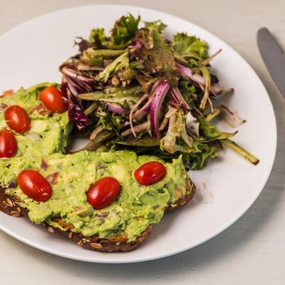 Avocado toast topped with grape tomatoes, served with side green salad.