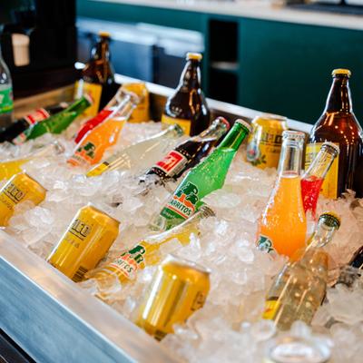 Variety of bottled and canned soft drinks chilling in an ice-filled metal trough.