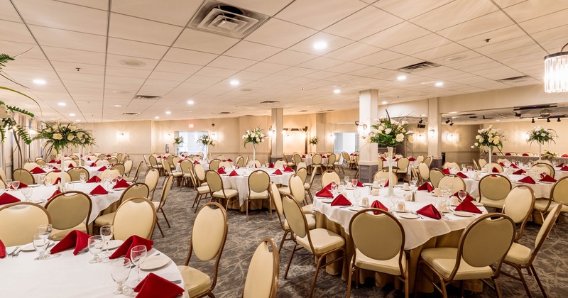 A banquet hall with round tables covered in white cloths, red napkins