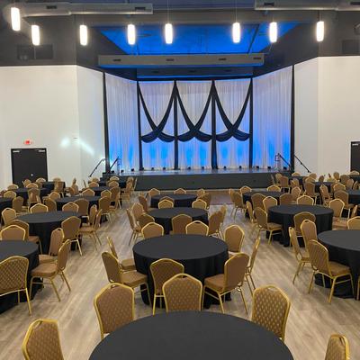 Lots of skirted round tables with chairs in front of the stage.