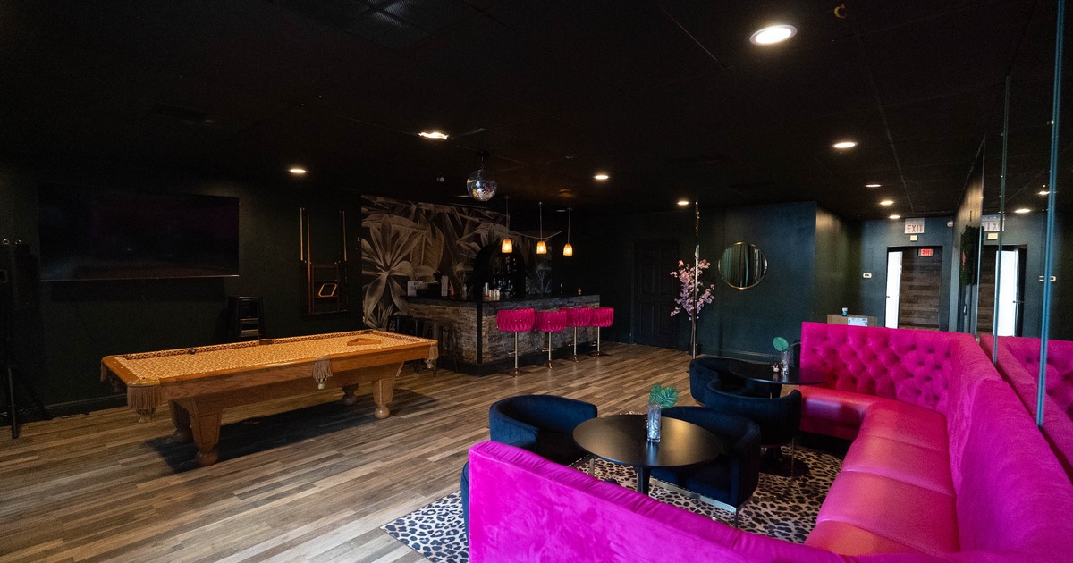 A modern lounge area featuring a pink tufted sofa, a wooden pool table, black lounge chairs