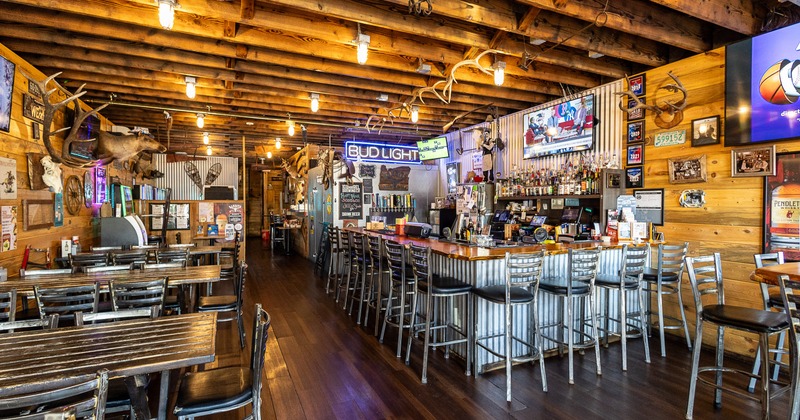 Spacious and rustic interior space, seating area with wooden tables and chairs, and bar with stools