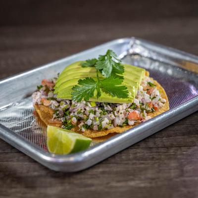 Ceviche tostada topped with avocado slices and cilantro.