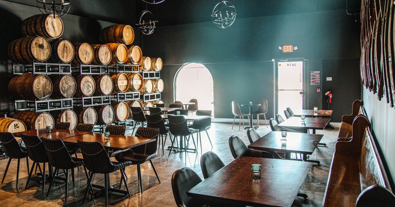 A room with tables, chairs and barrel racks lit by daylight coming through windows