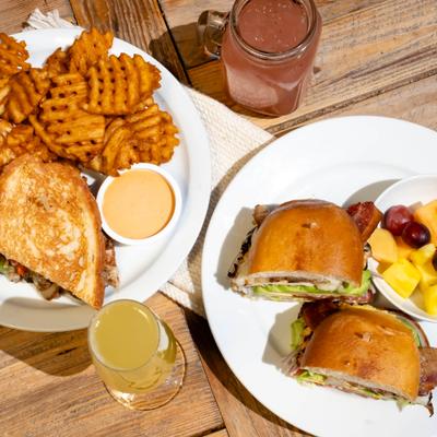 Philly cheesesteak melt with waffle fries and chicken club sandwich with fruit and drinks.