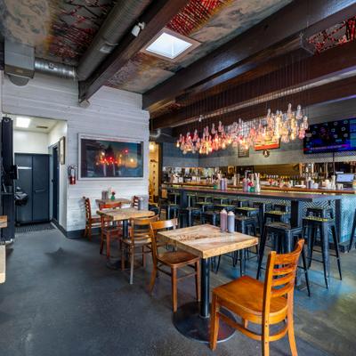 Interior with exposed ceiling pipes, wooden tables and a bar area with hanging lights.