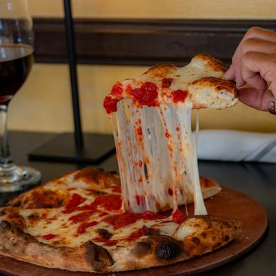 Slice of pizza being lifted from the whole pizza on a wooden tray.
