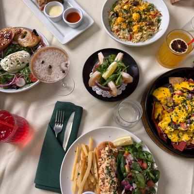 Assorted dishes and cocktails on a table including nachos, fries, lobster roll, and shrimp cocktail.