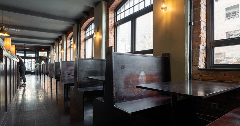 Interior of a restaurant with dark wooden booths and large arched windows