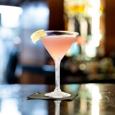 Pink colored cosmo cocktail, served in a martini glass with lemon garnish.
