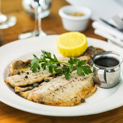 Branzino topped with fresh herbs and capers, served with a dressing and lemon.