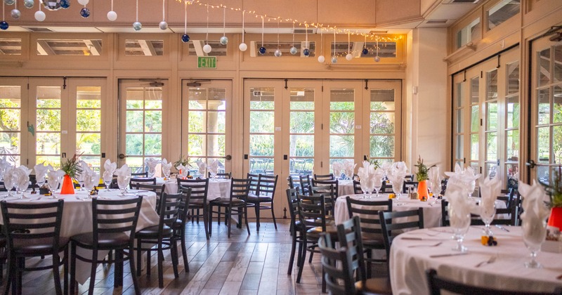 A banquet room with round tables covered in white tablecloths, dark chairs