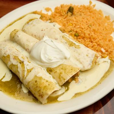 Enchiladas topped with green tomatillo sauce and cheese dip, served with rice.