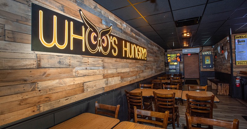 Rustic interior - wooden tables, chairs and illuminated sign "WHO'S HUNGRY?" on wood-planked wall