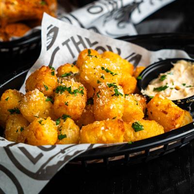 Tater tots garnished with herbs and a sprinkle of parmesan, served with a dip.