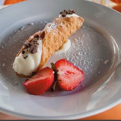 Cannoli dusted with sugar alongside a sliced strawberry.