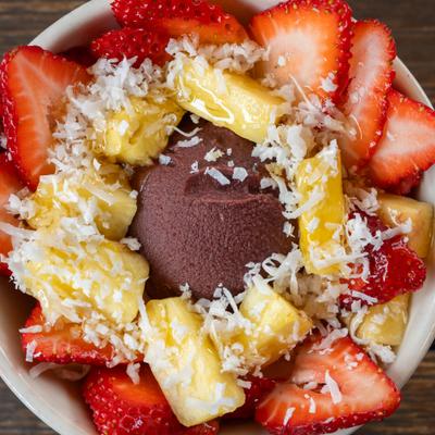 Acai bowl with bananas, strawberries, coconut flakes, and chocolate ice cream.