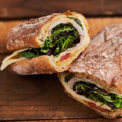Sandwich with meats,cheese and greens on a rustic bread.