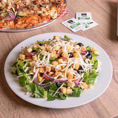 Garden salad topped with shredded cheese, black olives, and croutons on a white plate.