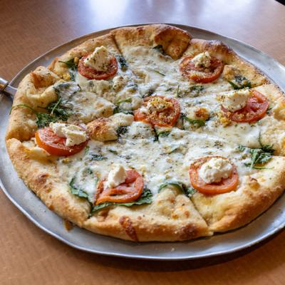 White margherita pizza topped with melted mozzarella, tomato slices, and fresh basil on a metal tray.