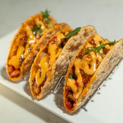 Three cheese-filled tacos on a white plate with a metal holder.