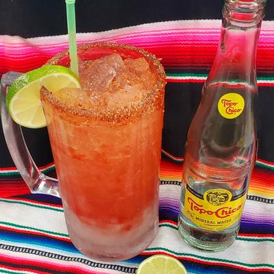 Michelada and a bottle of mineral water on a Mexican sarape blanket.