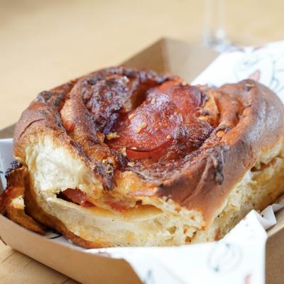A golden-brown pepperoni scroll sits in a cardboard tray.