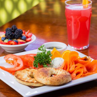Smoke Trout Bagel served with fresh fruit and a glass of red beverage.