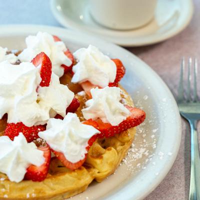 Belgian waffle topped with fresh strawberries and whipped cream.