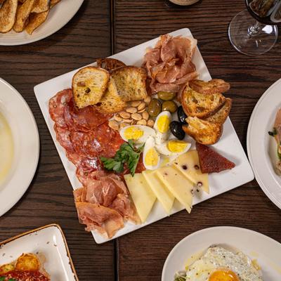 Antipasti plate on a wooden table surrounded by various dishes and wine.