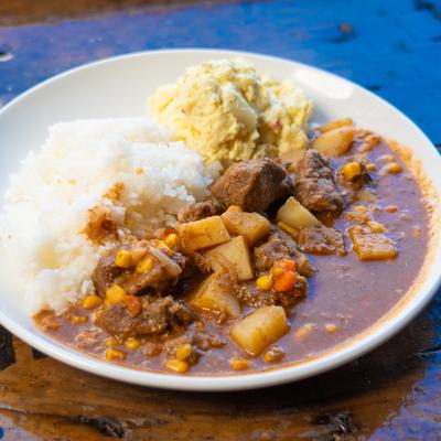 Beef stew served with rice and a side of potato salad on a white plate.