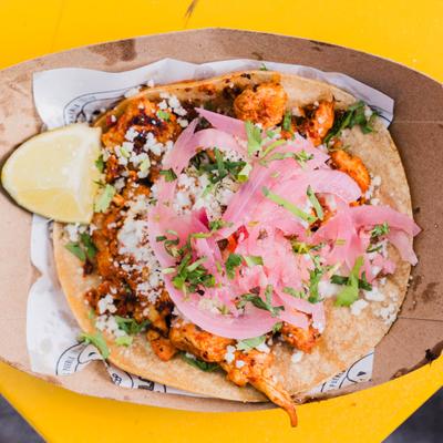 Chicken taco topped with crumbled cheese and pickled red onion.