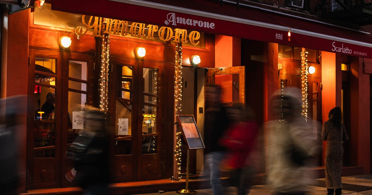 Restaurant exterior at night with red awning, warm lights, and people walking past