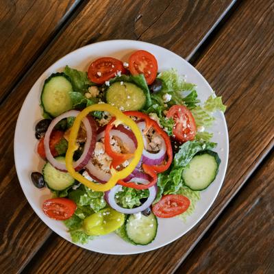 A fresh Greek salad with crisp cucumbers, tomatoes, peppers, and red onion rings.