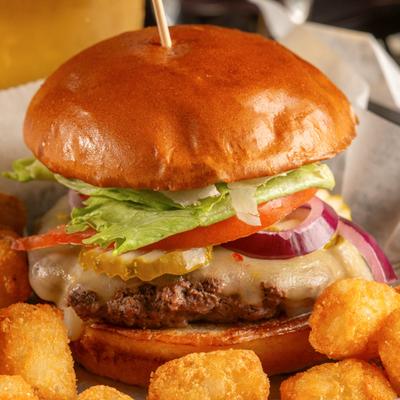 A cheeseburger with lettuce, tomatoes, and onions, served with tater tots.