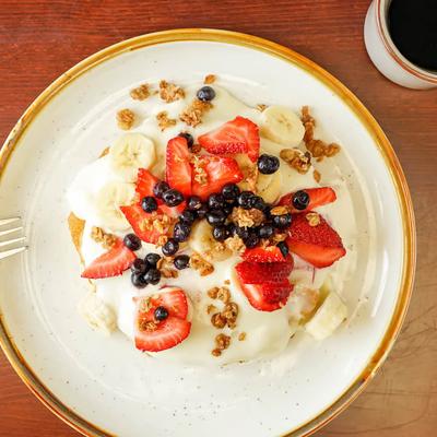 Pancakes topped with cream cheese, mixed berries, banana, and granola.