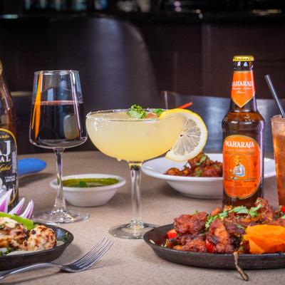 Indian beers, cocktails, and sizzling appetizers are spread across a restaurant table.