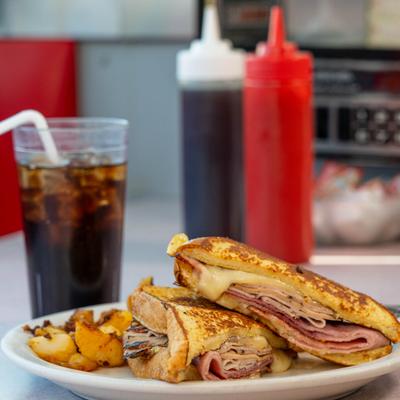 Monte Cristo sandwich served with home fries, alongside a drink.