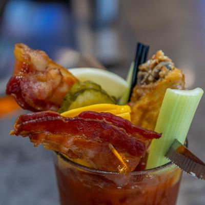 Bloody Mary cocktail garnished with bacon, chicken wing, pickles, cheese, and a celery stalk.