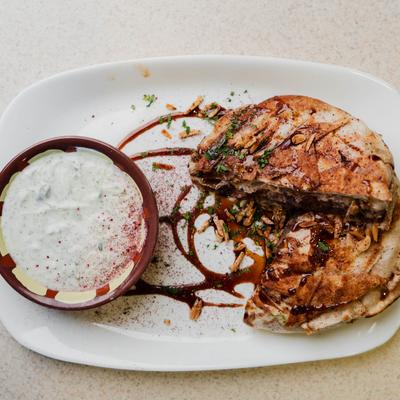 Palestinian chicken flatbread drizzled with sauce, accompanied by a creamy yoghurt dip.