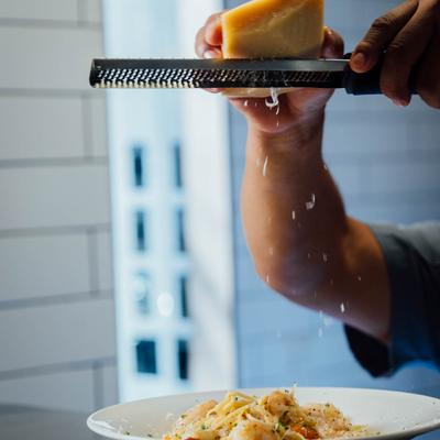 Kitchen staff member grating parmesan cheese on a dish