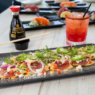 Thin crispy tuna pizza topped with onions, jalapeños, and cheese near a cocktail.
