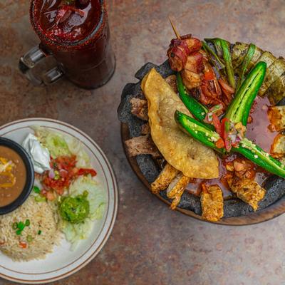 Molcajete served with rice, guacamole, sour cream, fresh salsa, and a Michelada.
