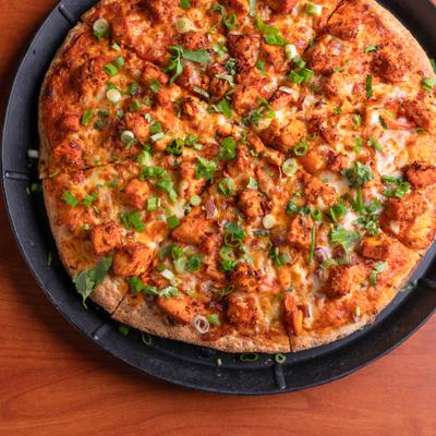 Pizza with garlic sauce, red onions, diced tomatoes, chicken tikka and green onions.